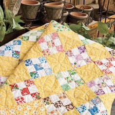 a yellow quilt is sitting on a table next to potted plants and other pots