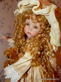 a close up of a doll with curly hair holding a teddy bear in her arms