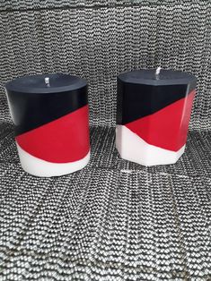 two candles sitting next to each other on top of a cloth covered surface with black, red and white stripes