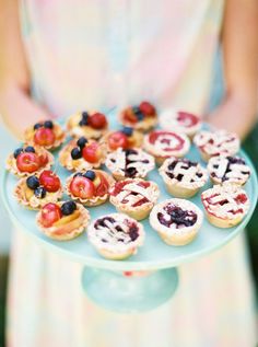 a person holding a plate with mini pies and berries on it in the shape of pretzels