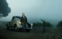 a man sitting on the hood of a pick up truck in front of a vineyard