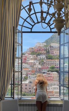 a woman standing in front of a window looking out at the city