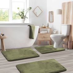 three green bathroom rugs in front of a white bathtub and toilet with wooden floors