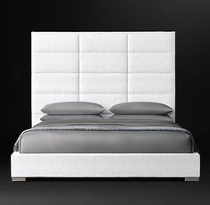 a white bed with grey sheets and pillows on it's headboard, against a black background