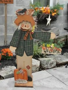 a scarecrow is standing in front of a welcome sign and pumpkins on the ground