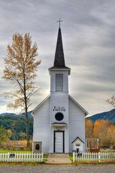 an old white church with a steeple on the top and a cross at the front