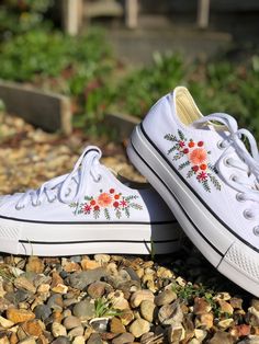 two white shoes with flowers painted on them are sitting on the ground next to some rocks