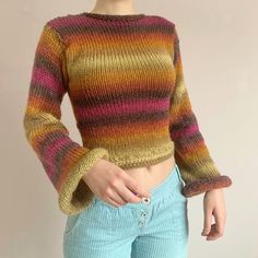 a woman wearing a multicolored sweater and blue jeans stands in front of a white wall