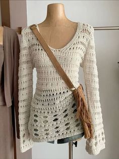 a white crocheted sweater with tassels and a cross body bag on a mannequin