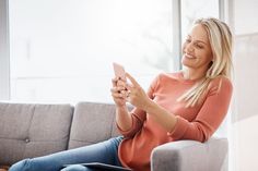 a woman sitting on a couch looking at her cell phone and smiling as she sits down