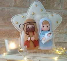 two nativity figurines sitting on top of a mantle next to a lit candle