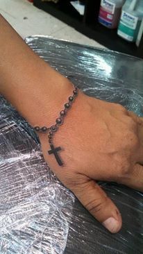 a person's hand with a cross tattoo on it and a chain around the wrist