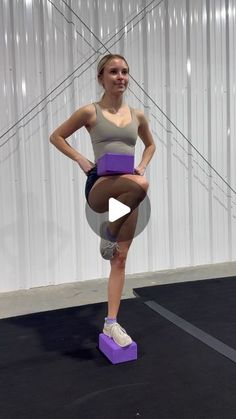 a woman standing on top of a purple block in front of a white wall and holding her hands behind her back