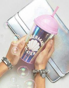 two hands holding a pink and blue cup next to a silver suitcase with the words mermaid water on it