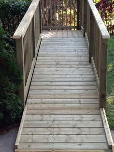 a wooden walkway leading up to a fenced in area with trees and bushes behind it