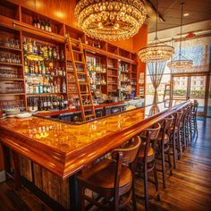 a bar with wooden shelves and stools next to a chandelier hanging from the ceiling