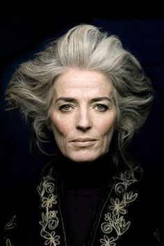 an older woman with grey hair and black shirt looking at the camera, in front of a dark background