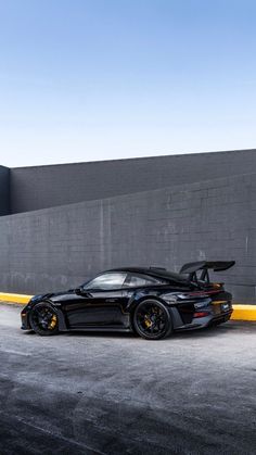 a black sports car is parked in front of a gray wall and some yellow poles