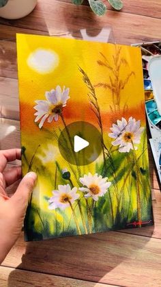 someone is holding up a painting with daisies on it