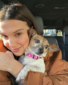 a woman holding a small dog in her lap while sitting in the back seat of a car