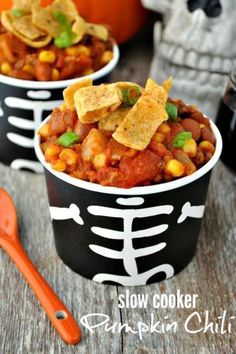 two black and white bowls filled with chili, beans and tortilla chips on top of a wooden table