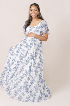 a pregnant woman in a blue and white floral print dress, smiling at the camera