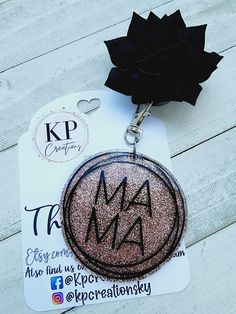 a key chain with the word ma on it and a black flower attached to it