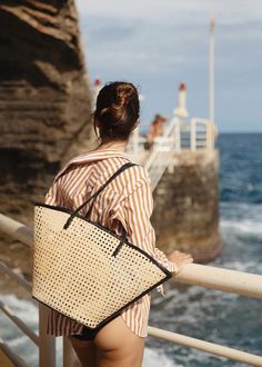 A beach bag to plan a vacation for. Lou is the ultimate summer tote. Made in our signature cane rattan with leather details that elevate it to a handbag. The structured base keeps Lou upright on the sand, so your belongings stay sand-free (as long as no one's tossing pétanque nearby!) and the wider opening gives you extra room for your beach essentials. Pairs perfectly with ocean salty hair and tan lines. Also available in Caramel Rattan. Woven rattan Cow leather straps, trim and base | Magnetic Travel Bags With Bamboo Handle For Beach Season, Straw Beach Bag With Bamboo Handle For Travel, Chic Sand-colored Straw Tote Bag, Casual Beach Bag With Bamboo Handle For Travel, Beach Tote Bag With Bamboo Handle, Beach Tote Bag With Bamboo Handle For Beach Season, Beach Season Tote Bag With Bamboo Handle, Natural Bags With Bamboo Handle For Day Out, Chic Beach Bag With Bamboo Handle