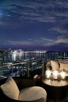 a balcony with wicker furniture and lanterns lit up at night overlooking the city lights