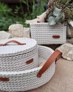 two woven baskets with leather handles are sitting on the ground next to rocks and plants