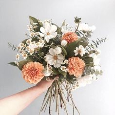 a bouquet of flowers being held by someone's hand on a gray background with white and orange flowers