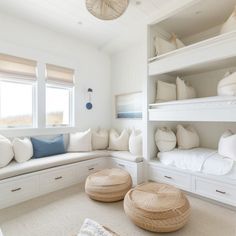 a room with white furniture and lots of pillows on the windowsills, along with two large round stools