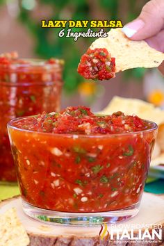 a person dipping salsa into a glass bowl with tortilla chips on the side