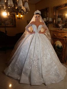 a woman in a white wedding gown standing next to a mirror and chandelier