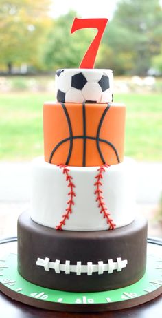 a three tiered cake with a basketball and soccer ball on top