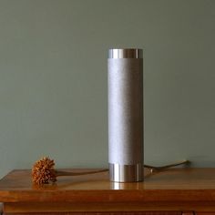 a silver cylinder sitting on top of a wooden table next to a small pine cone