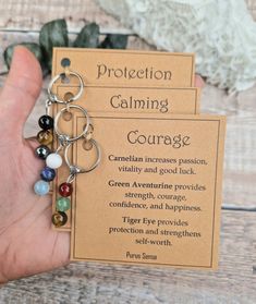 a person holding two key chains with the words protection, calming and courage on them