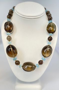 A gorgeous color pairing of warm toffee brown with cool sea glass blue is mesmerizing in this sophisticated and eye-catching necklace that combines smoky quartz with aquamarine and 18k yellow gold. Large, smoky quartz oval crystals have been polished to a glistening smooth finish and make a bold statement of refinement and luxury as they stand out against smaller smoky quartz beads and bright aquamarine spacers. This necklace will transition easily between day and night, and looks casually elega Large Crystal Necklace, Luxury Brown Beaded Necklaces With Round Beads, Luxury Brown Beaded Necklaces, Elegant Style, Wooden Bead Jewelry, Smoky Quartz Jewelry, Gold Beaded Necklace, Vintage Jewelry Ideas, Creative Necklace, Resin Jewelry Diy