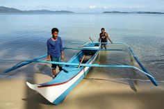 two men standing next to a boat on the beach