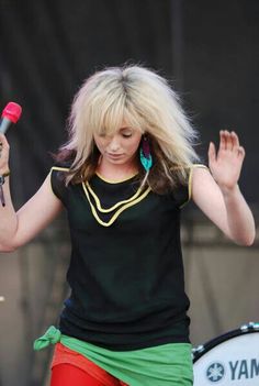 a woman with blonde hair is holding a microphone and wearing red pants while standing on stage