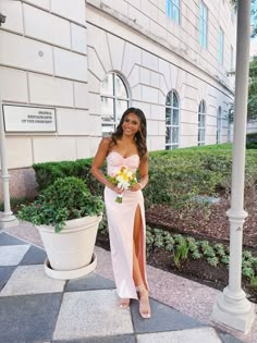 a woman standing in front of a building wearing a pink dress and holding a bouquet