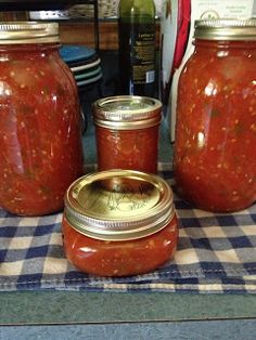 three jars filled with red sauce sitting on top of a checkered table cloth next to bottles