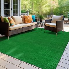 a living room area with green carpet and couches on the outside patio, looking out onto trees