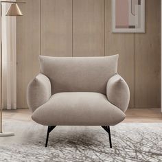 a beige chair sitting on top of a white rug next to a lamp and painting