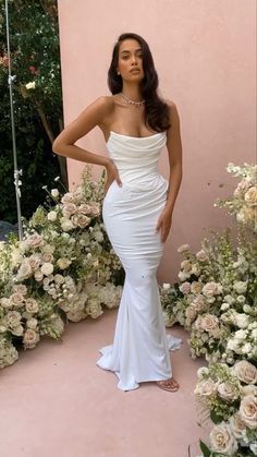 a woman standing in front of flowers wearing a white dress