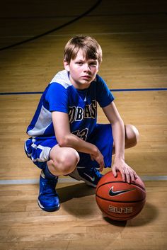 a young boy kneeling down next to a basketball