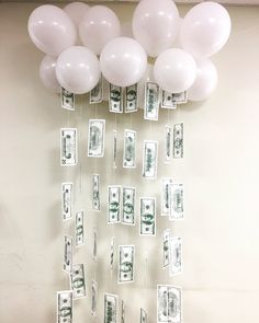 balloons and money are hanging from the ceiling in front of a wall with white balloons