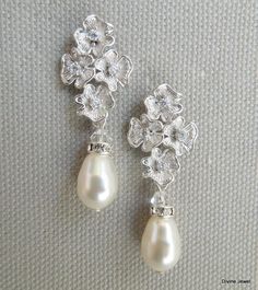 "These elegant earrings have small flower pendants in matte rhodium plated finish and Swarovski teardrop pearls. Ivory/cream Swarovski pearls measure 11 mm long. Earrings are approximately 1 1/2\" long from top to bottom by 1/2\" wide. Each flower has a tiny clear cubic zirconia in the center. Post is .925 sterling silver over brass. Please choose desired pearl color and finish at checkout. Perfect for any nature inspired bride! Matching necklace, https://www.etsy.com/listing/274801382/backdrop- Pearl Drop Dangle Clip-on Earrings For Wedding, Silver Teardrop Pearl Bridal Earrings, Teardrop Pearl Embellished Earrings For Wedding, Silver Pearl Teardrop Bridal Earrings, Silver Teardrop Bridal Earrings With Pearl Charm, Teardrop Pearl Embellished Bridal Earrings, Teardrop Pearl Bridal Earrings For Wedding, Elegant Teardrop Pearl Drop Bridal Earrings, Pearl White Clip-on Earrings With Pearl Drop For Wedding