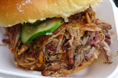 a pulled pork sandwich with pickle slices in a white container on a table top