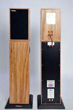 two wooden speakers on black stands against a white background with a note attached to it